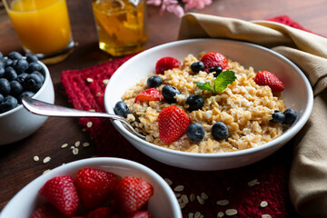 Creamy oatmeal, blueberries and strawberries in a bowl with honey and orange juice