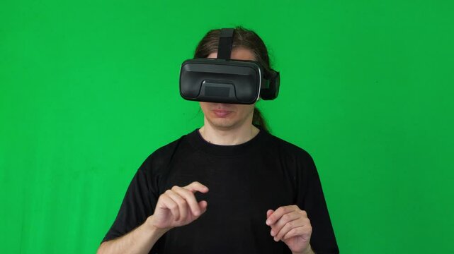 A mid-shot captures an interactive and engaging mood as a person wearing a VR headset makes open-hand gestures, suggesting immersion in a virtual environment or game, against a green screen background