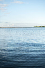 Serene landscape featuring a lake with gentle ripples on the surface and a distant shoreline under a clear sky. 