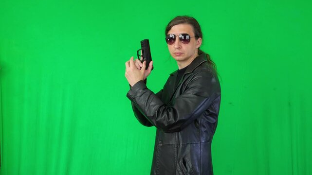 A mid-shot captures a serious and vigilant mood as a man in a leather jacket and sunglasses holds a handgun, looking to the side, ready for action, against a green screen