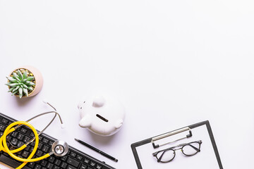 Creative flat lay overhead view with keyboard, medical stethoscope, piggy bank, succulent flower...