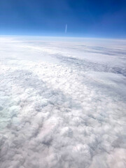 Naklejka premium A scenic view from the airplane window showing soft white clouds and the earth far below. The altitude offers a breathtaking perspective of the landscape and sky