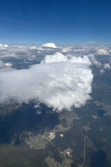 A scenic view from the airplane window showing soft white clouds and the earth far below. The altitude offers a breathtaking perspective of the landscape and sky