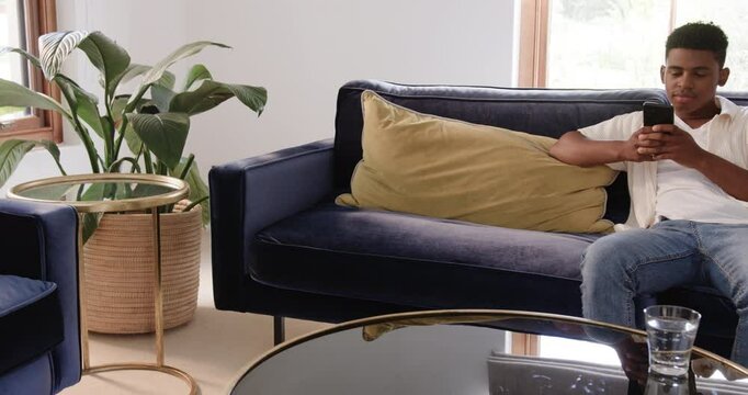 Diverse male friends receiving envelope on couch, unfolding letter to inspect contents and smiling