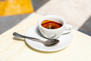 Close-up of a freshly brewed espresso in a white cup with a spoon on a saucer.