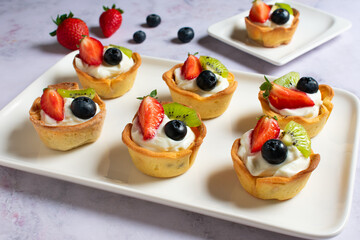 Tartaletas de crema de queso y fruta fresca en bandeja de cerámica blanca