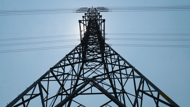 A towering electricity pylon against a clear blue sky, showcasing the structure's intricate metal framework and overhead power lines.