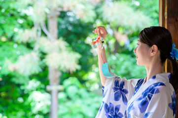 浴衣姿の女性が夏の風鈴を見つめる静かな日常の一コマ