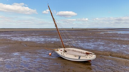 Tilted sailboat resting on muddy flats under calm sky on British coastline.