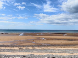Sweeping view of empty beach, blue skies and sea with distant horizon and clouds.