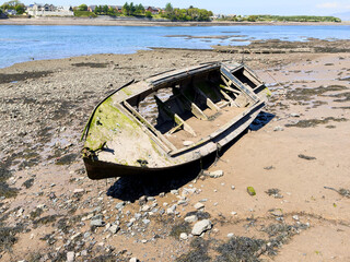 Weathered fishing boat decaying on a tidal estuary shore in bright sunlight.