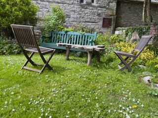 Quaint garden scene with rustic wooden table and vintage chairs near a stone wall.