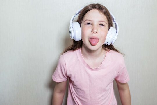 Funny teen girl in headphones shows her tongue and looks at the camera, cooy space