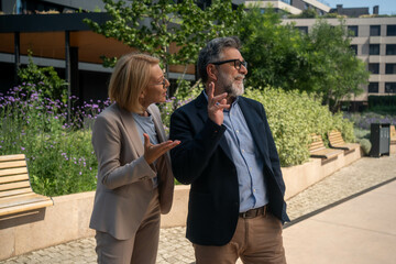 Frustrated mature businesswoman arguing with dismissive businessman outdoors in modern corporate district