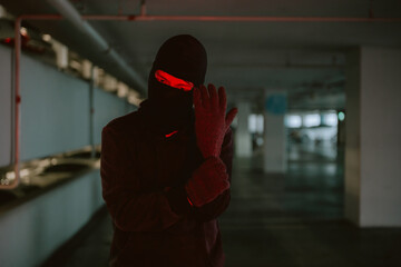Mysterious figure dressed in black stands ready for action in a dimly lit parking garage at night