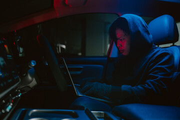 Young person focused on laptop inside a dark car during nighttime surrounded by dim blue and red...