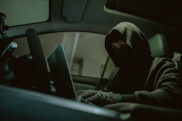 Intruder works on laptop inside a parked car at night in a dimly lit area