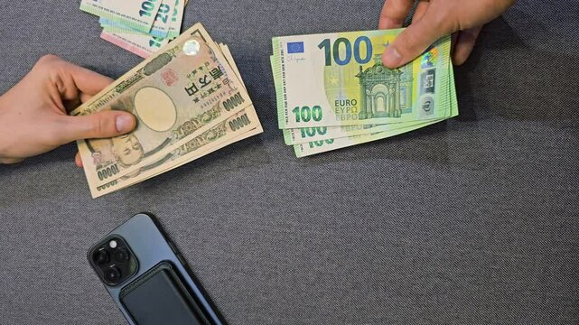 Hands holding euro banknotes and Japanese yen cash on table with smartphone close up top view international currency exchange payment and global financial transaction concept
