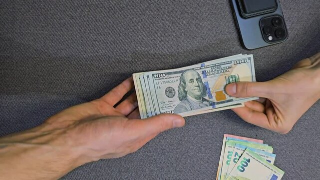 Hands holding and counting US dollar banknotes with euro cash and smartphone on table close up top view currency exchange payment and financial transaction concept