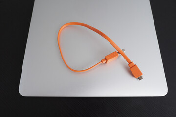 Charging micro usb cable in bright orange color placed on a sleek silver laptop surface.