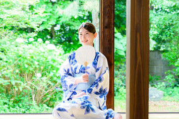 団扇を持ち緑の庭を背景に涼を感じる浴衣姿の女性