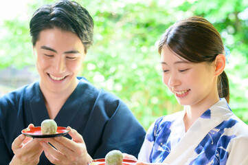 浴衣姿の男女が和菓子を見せ合う和やかな夏のひととき