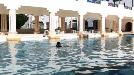 Calm morning swim in a resort pool soft ripples reflect bright sunlight elegant arches peaceful retreat cool water and relaxed luxury in a quiet Mediterranean-style courtyard - Powered by Adobe