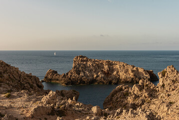 Coast of Menorca, rocks, small island, and sailing boat.