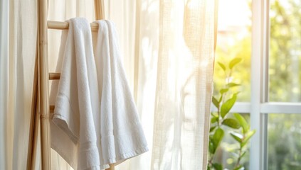 White towels hanging on a light wooden ladder leaning against a sheer window. Sunlight streams through the window
