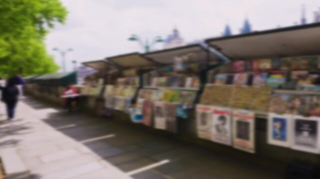 People stroll along the Quai de la Megisserie embankment in spring past green metal kiosks with souvenirs and posters. Out of focus. Paris, France.