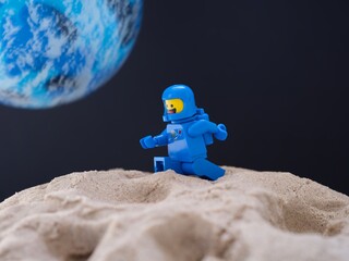 Obraz premium Tambov, Russian Federation - July 28, 2024 Blue Lego astronaut minifigure walking on sand on a planet against black space background with another blue planet in it