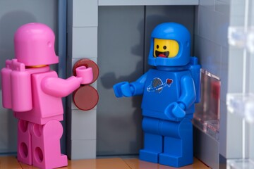 Obraz premium Tambov, Russian Federation - May 26, 2025 Two Lego astronaut minifigures waiting at an elevator. The pink one is pressing a button on the elevator. Close-up