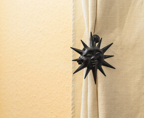 Sun Curtain Tieback. A decorative black sun-shaped curtain tieback holding back a beige curtain.