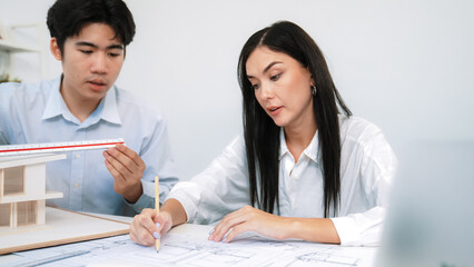 Professional male engineer measure house model by using ruler while beautiful cooperative coworker...