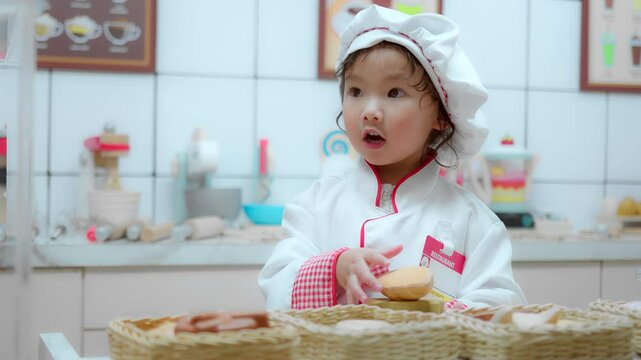 A cute child in a chef outfit curiously examines baked goods in a contemporary kitchen environment.