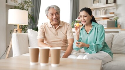 Happy elderly couple enjoying a ball toss game together at home, practicing coordination and cognitive skills for healthy aging. Grandfather and grandmother throwing ping pong in the bowl. Myrmidon.