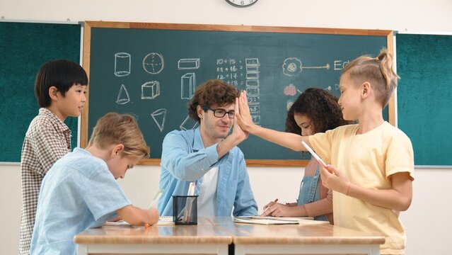 Caucasian teacher giving high five to encourage children to working together. Group of diverse student high five with instructor and present classwork while drawing and writing mind mapping. Pedagogy. - Powered by Adobe