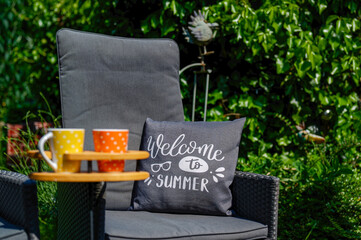 Scene with two coffee cups in a special wooden cup holder, a chair and a cushion in a garden.