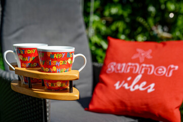 Scene with two coffee cups in a special wooden cup holder, a chair and a cushion in a garden.