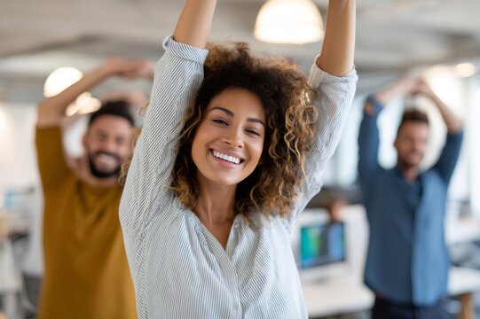 Smiling businesswoman stretching with arms raised in office with coworkers