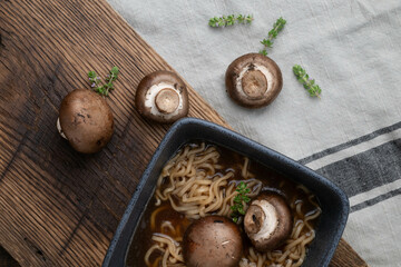 Whole baby portobello mushrooms and fresh thyme on a rustic wooden cutting board with a bowl of...
