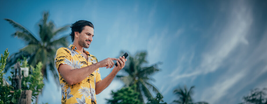 A contented man is standing with a phone in his hands on a background of palm trees.