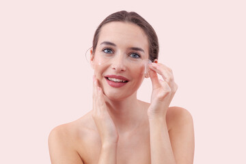Portrait of happy young woman with a natural, no makeup look, applying silicone under eye patches...
