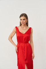 Woman in a red sleeveless dress with a deep V-neckline stands confidently, wearing minimal jewelry. Her straight hair is worn down, and she gazes slightly to the side