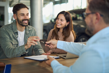 Happy couple about to sign a contract on a meeting with car salesperson in a showroom. 