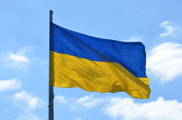 Yellow-blue flag of Ukraine as a symbol of the country flutters in the wind on background of blue sky with white clouds.