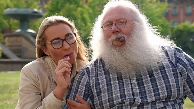 Elderly man with long beard and glasses shares a moment with a younger woman in a park during a sunny day, father and daughter, grandfather and granddaughter