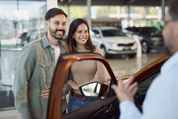 Happy couple communicating with car salesperson while buying a car in a showroom.	
