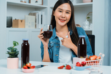 Smiling young beautiful Asian reviewing tasty mixed strawberry and cherry juice detox drinks,...