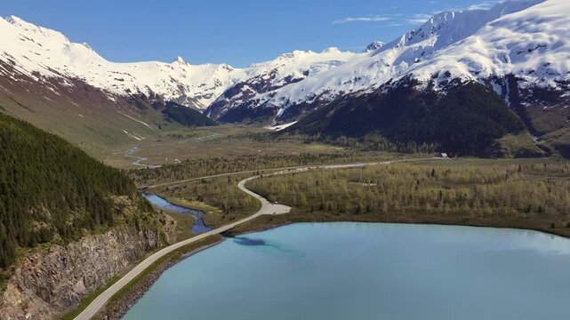 flying across Portage Lake along "Portage Glacier Rd toward toward "Anton Anderson Memorial Tunnel" entrance, snow covered mountain landscape surrounding the valley - 4k aerial video footage